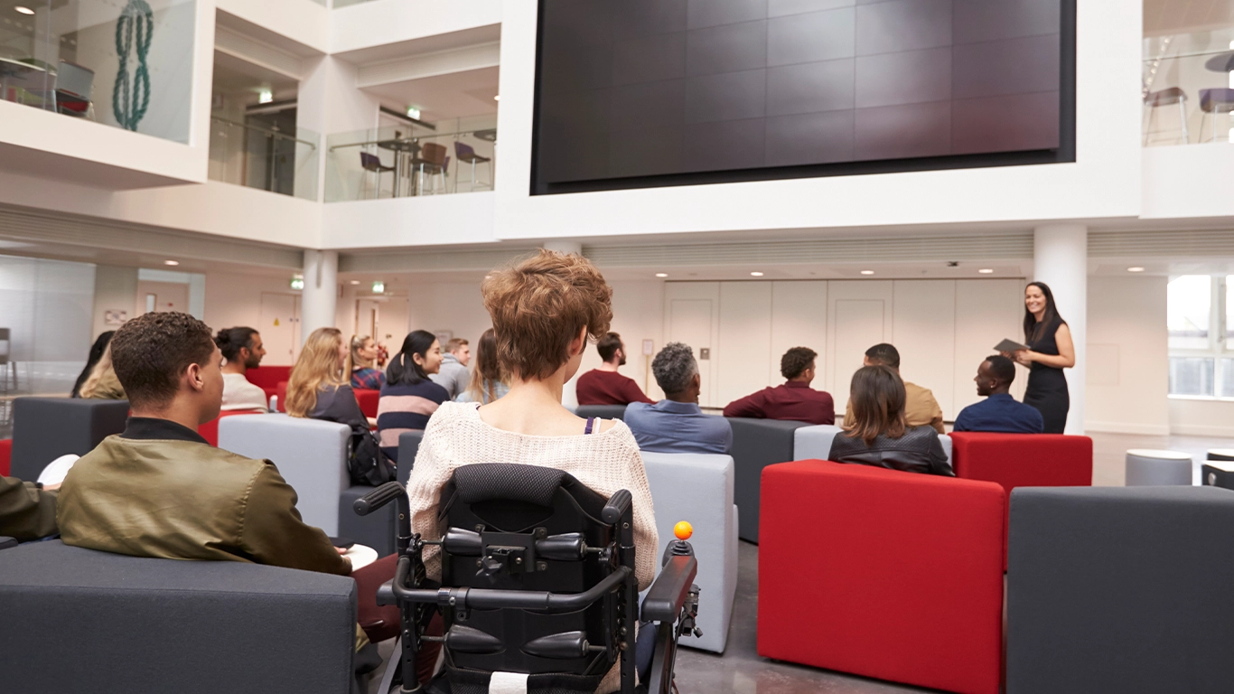 Teilnehmende sitzen in Reihen und verfolgen aufmerksam eine Präsentation bei einer Fachveranstaltung. Die Bühne ist gut beleuchtet, und der Vortragende spricht vor einer großen Leinwand