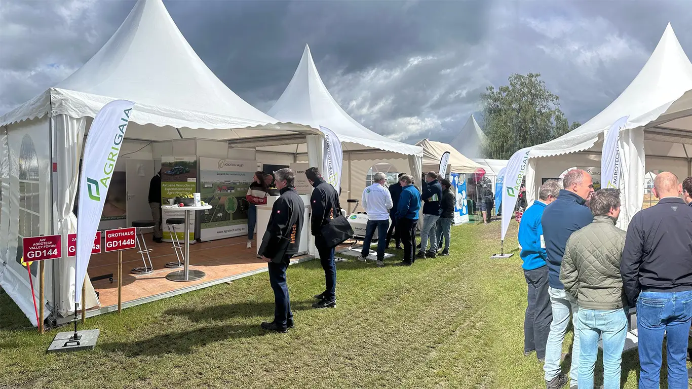 Außenbereich der DLG Feldtage mit weißen Pagodenzelten. Besucher informieren sich an den Ständen von Agri-Gaia und Agrotech Valley. Wind, Wetter und Natur bilden den typischen Rahmen für die Open-Air-Messe.